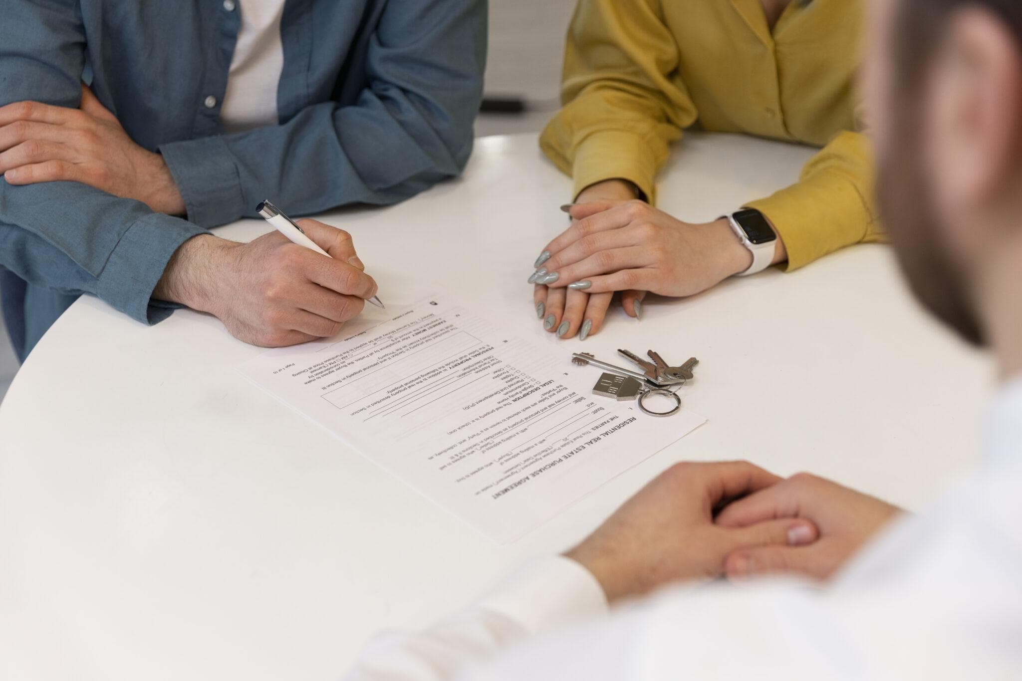 Two people signing mortgage documents beside a set of house keys