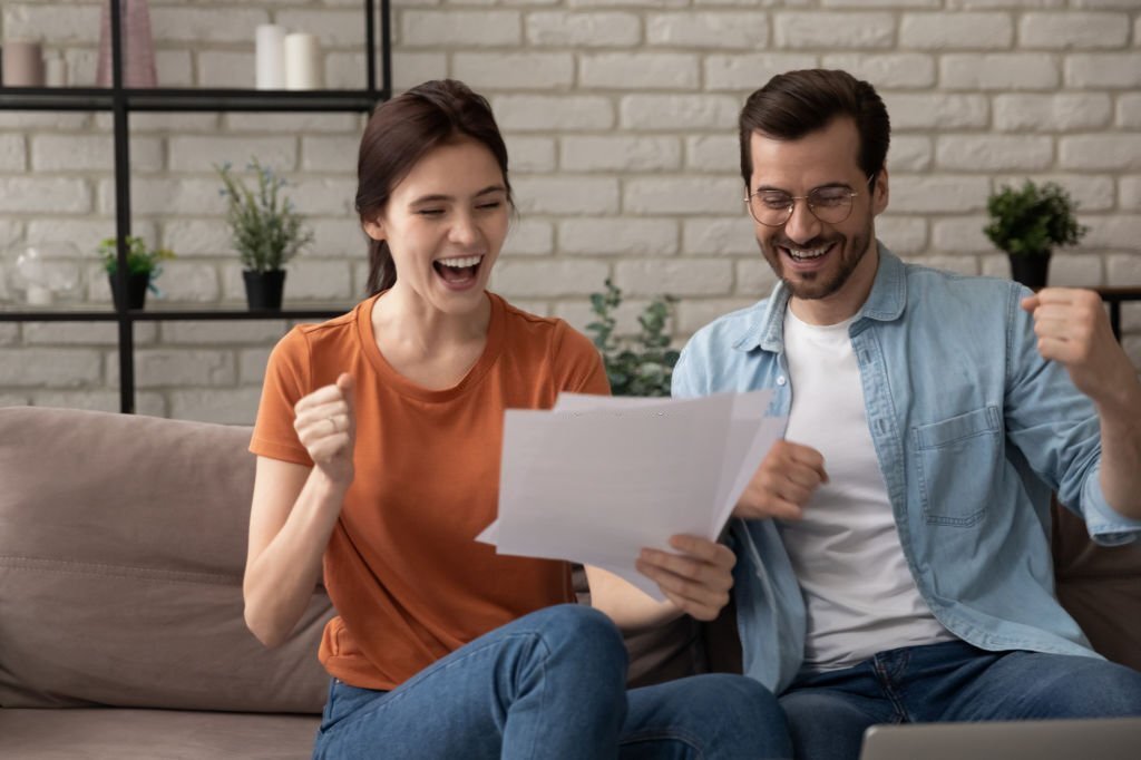 Excited young Caucasian man and woman spouses triumph get good pleasant news in postal letter correspondence, overjoyed millennial couple tenants or renters celebrate bank notice approval